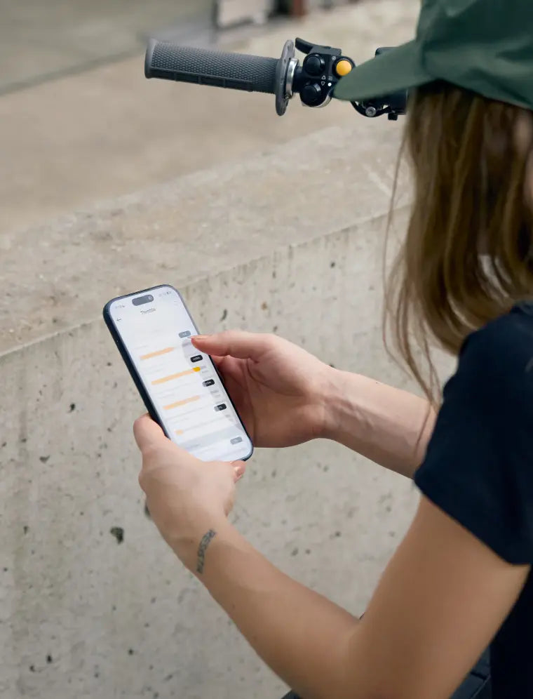 Rider adjusting throttle settings on a phone beside the bike